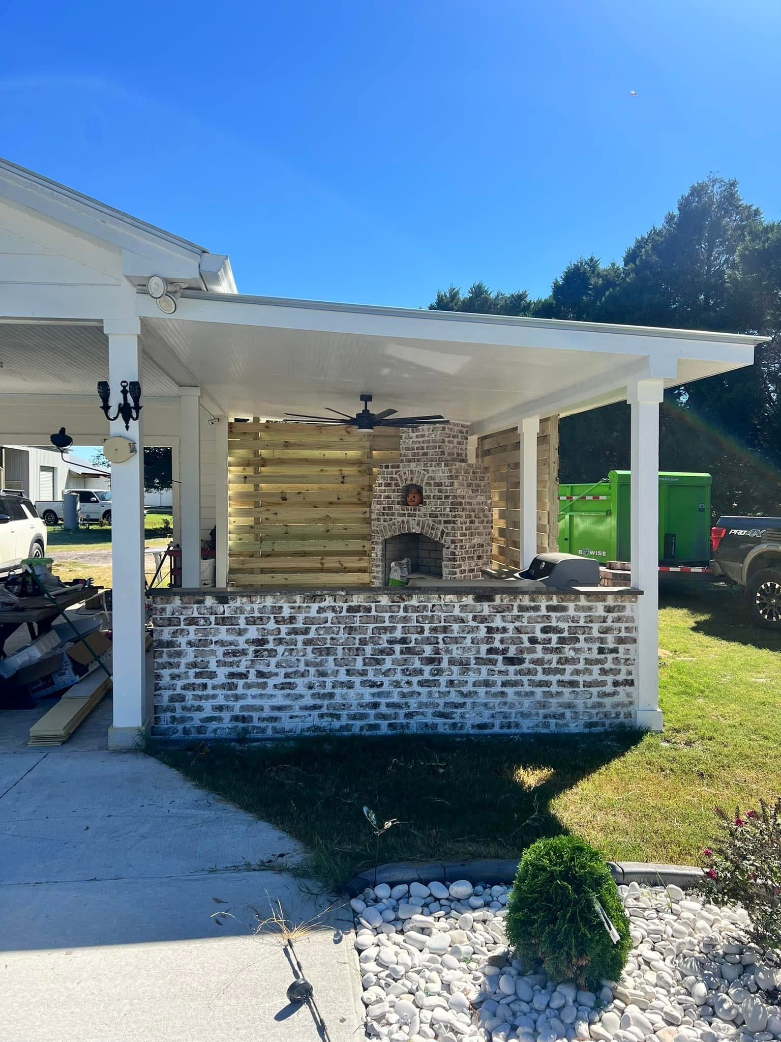 Covered outdoor kitchen with brick bar and masonry fireplace seen from the yard